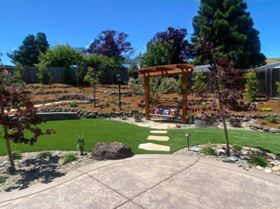 Completed backyard landscape with an arbor, lawn, stepping-stone path, trees, and natural stone
