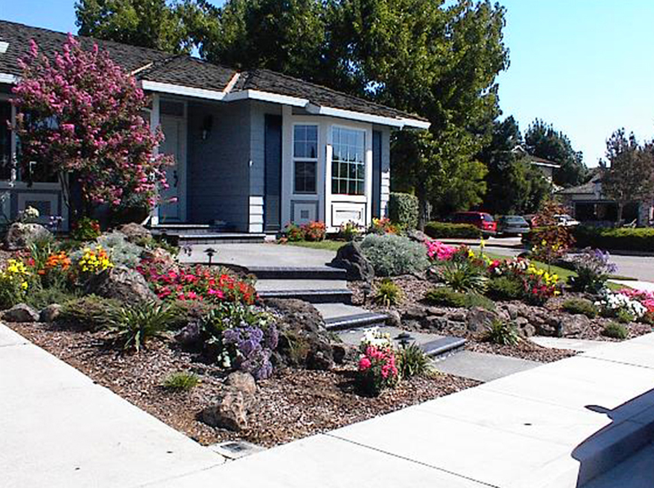 Colorful front-yard landscape with flowering plants, boulders, and a path leading to the home